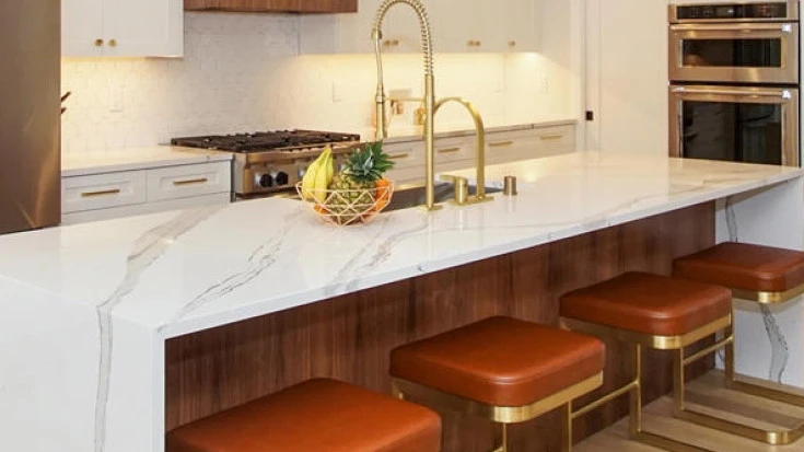 a bright white kitchen with Brittanicca quartz waterfall island and orange and gold island stools