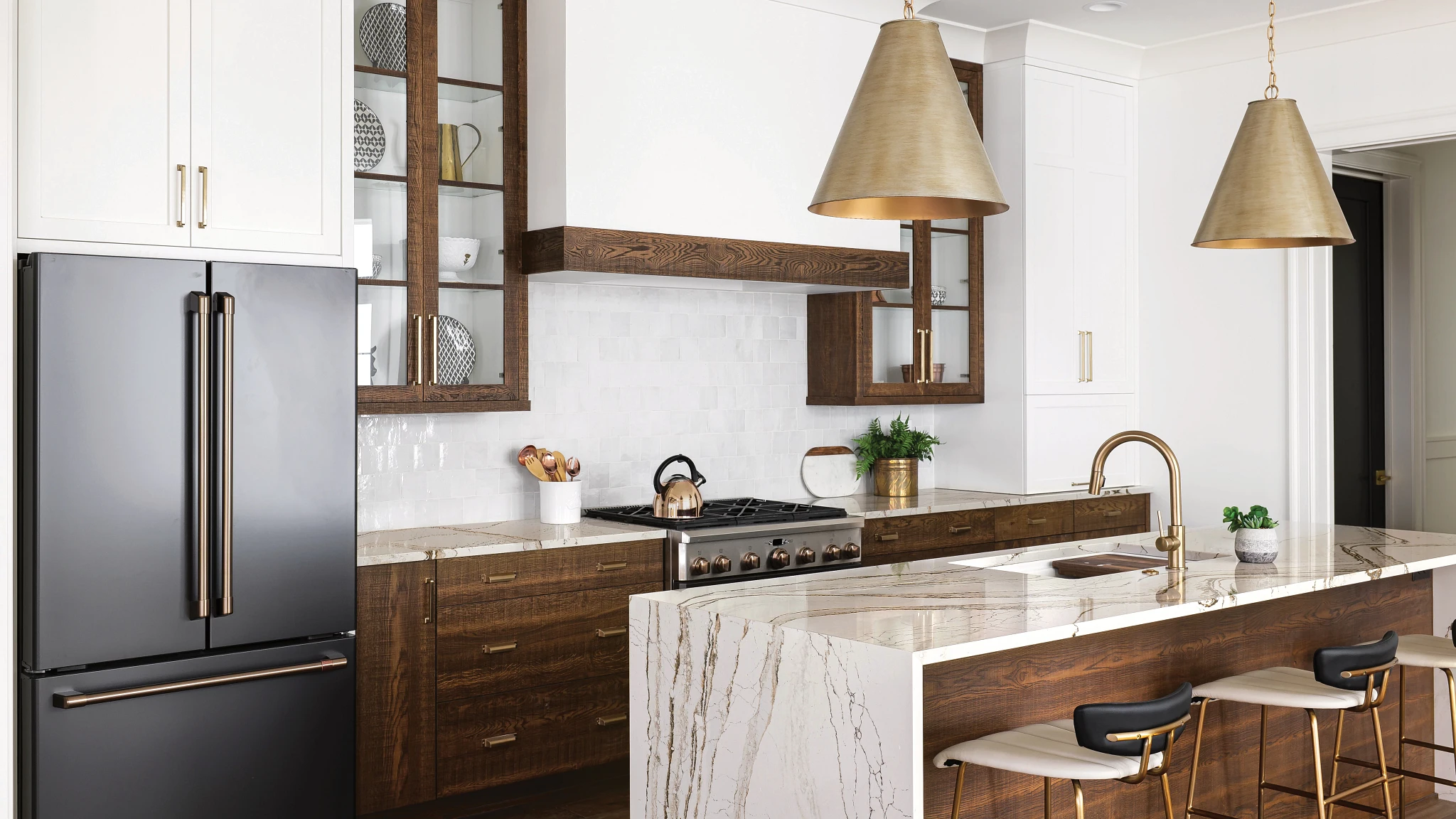 a modern, yet traditional kitchen with dark oak lower and upper cabinets, as well as oak island topped with white and brown quartz countertops, with black and gold accents throughout the kitchen. 