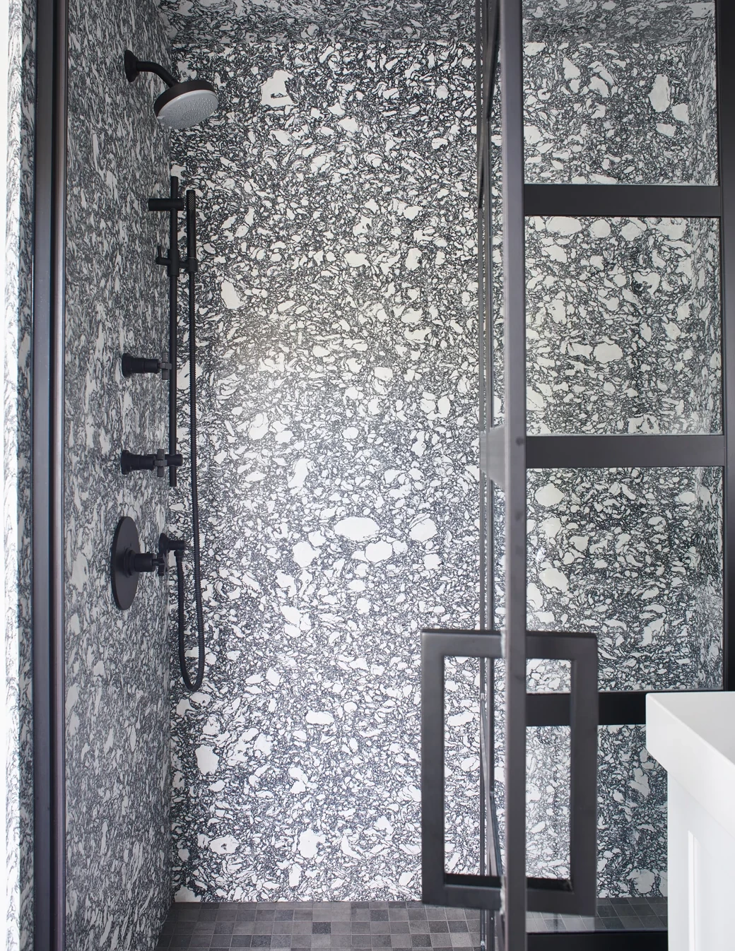 a primary bathroom with bold, black and white aesthetic and a mix of Cambria Rose Bay Matte and Cambria white Cliff Matte with gray floor tile and a black glass shower door.