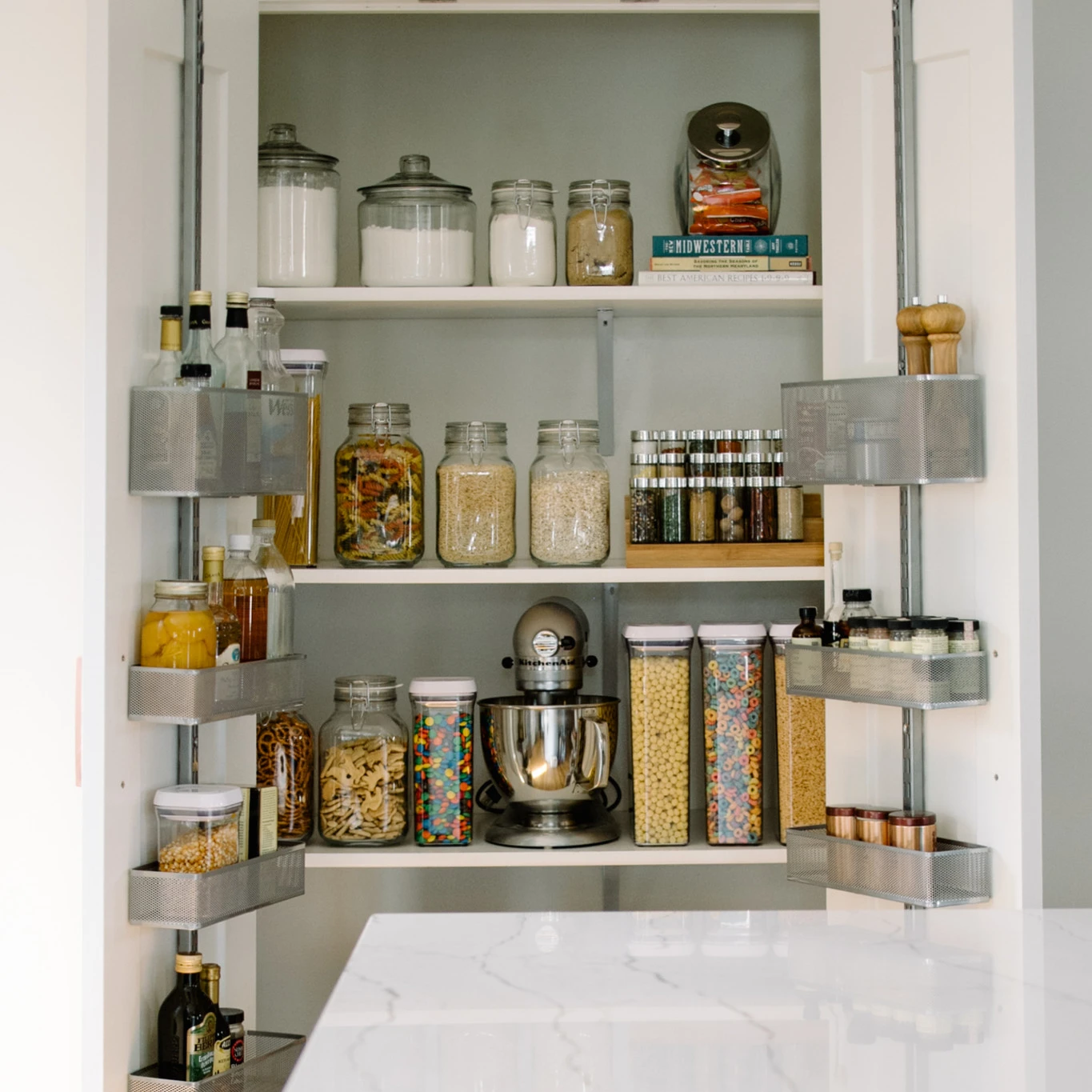 a organized pantry with jars and canisters to hold dry foods with a Ella quartz kitchen island