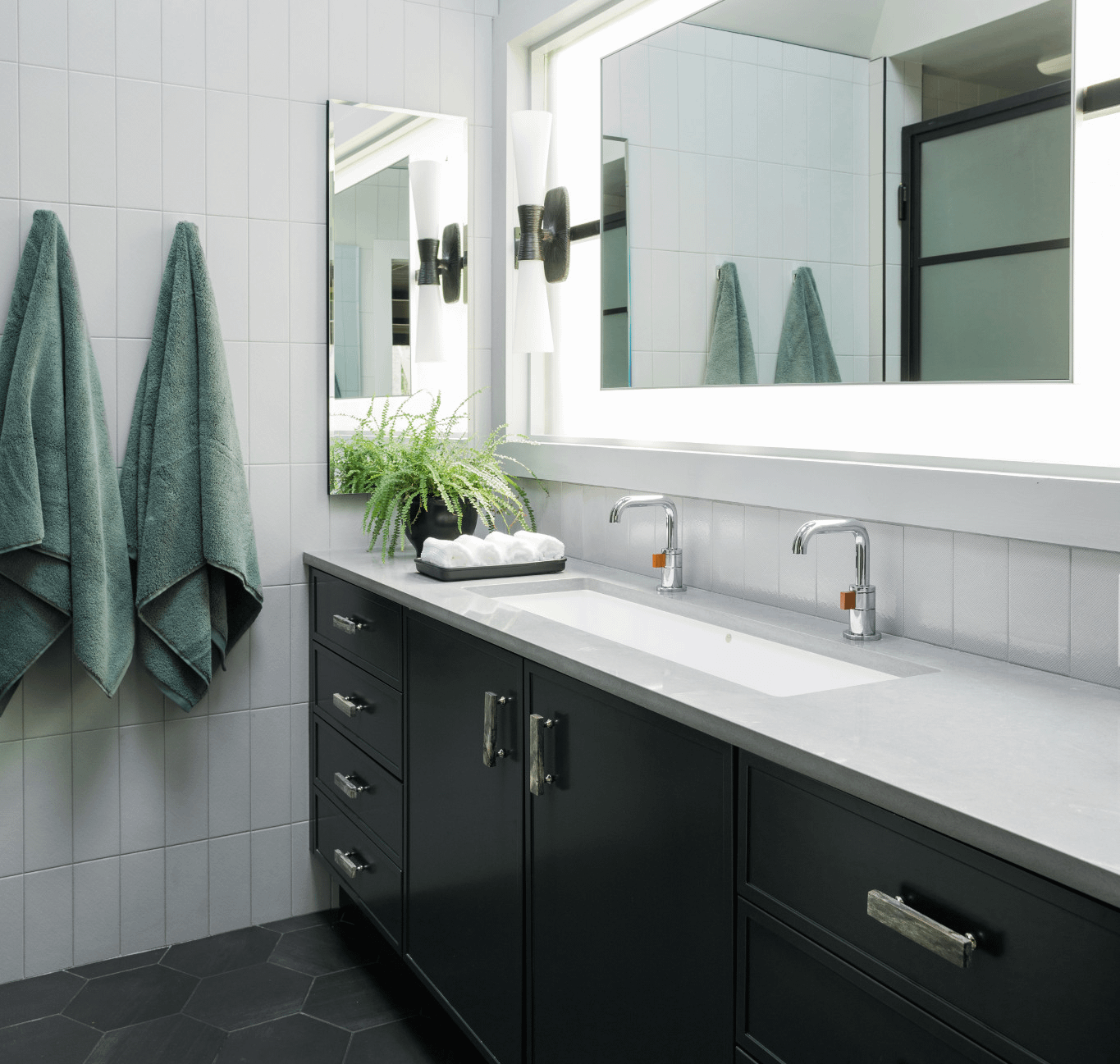 a clean and modern bathroom with black hexagonal floor tiles, black cabinets, white tile walls, a large mirror, and gray quartz countertops made from Cambria Carrick. 