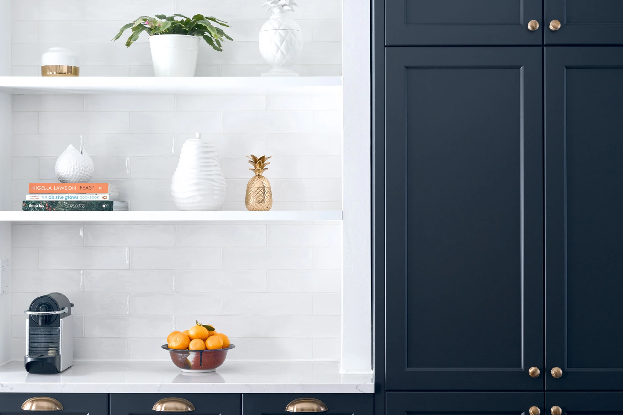 a white subway tile backsplash with open shelving and navy blue cabinets topped with Cambria Quartz Ella countertops.