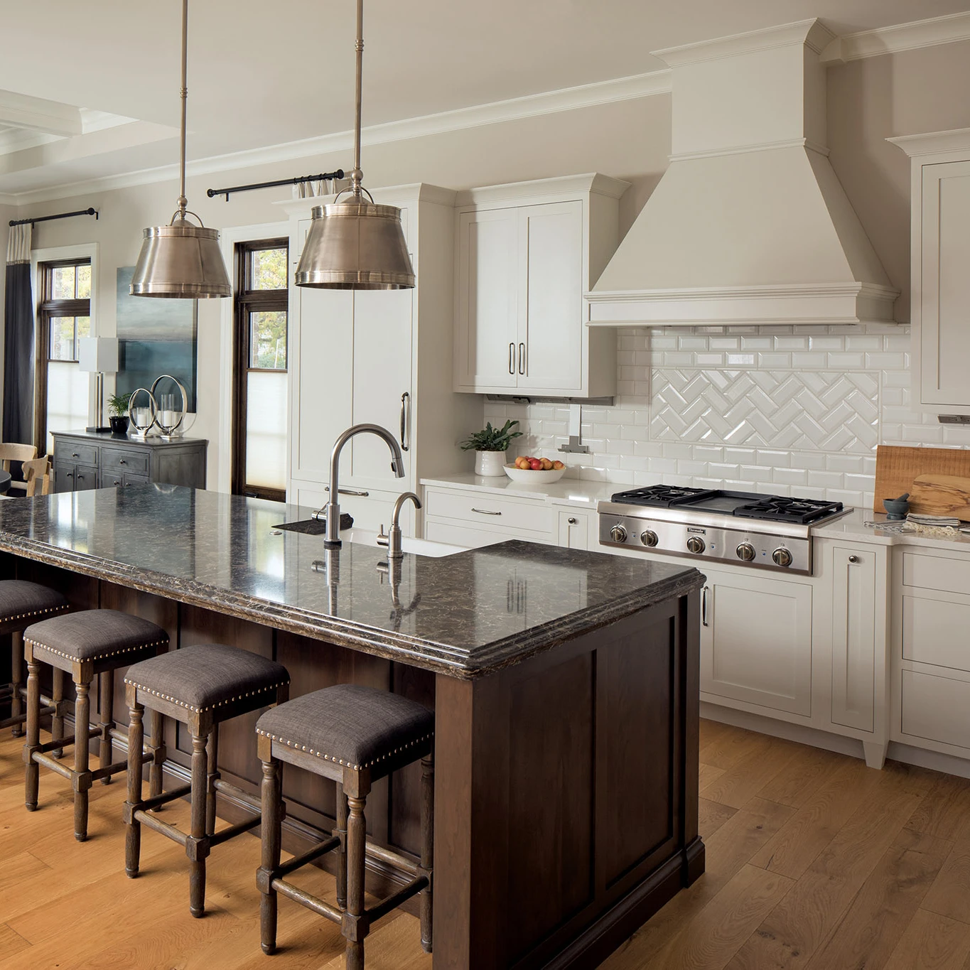a traditional kitchen with a dark oak island topped with Cambria Laneshaw quartz countertops paired with cream countertops and complemented with mixed metal light fixtures, faucet, and range.