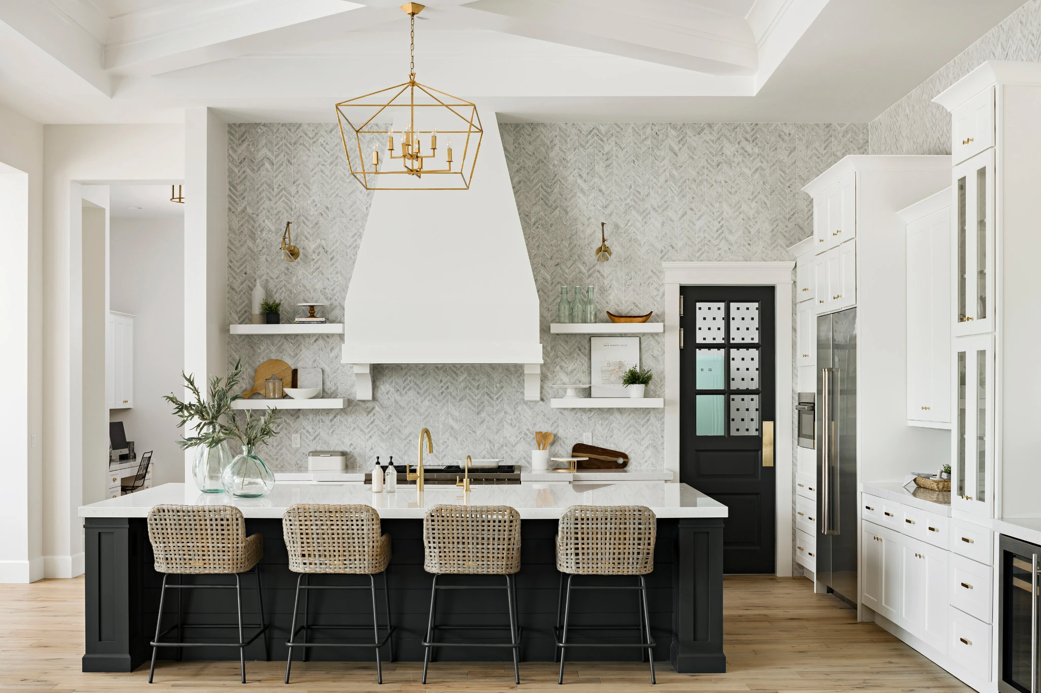 a bright white kitchen with large black island topped with Cambria Swanbridge white quartz countertops and gold accent features.