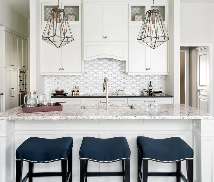 A white kitchen with Cambria Bellingham quartz kitchen island featuring three navy blue bar stools and eye-catching gold light fixtures.
