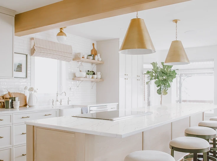 a kitchen with stained white oak cabinets topped with Cambria Quartz Ella countertops with brass accents in the ceiling beam and hanging ceiling lights.