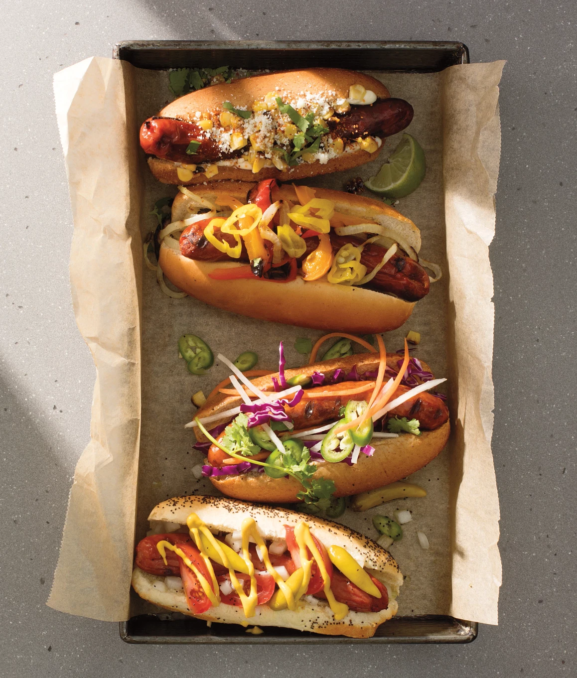 4 Chicago style hot dogs sitting in a tray lined with parchment paper on top of Cambria's Chicago Tower Matte quartz countertop. 