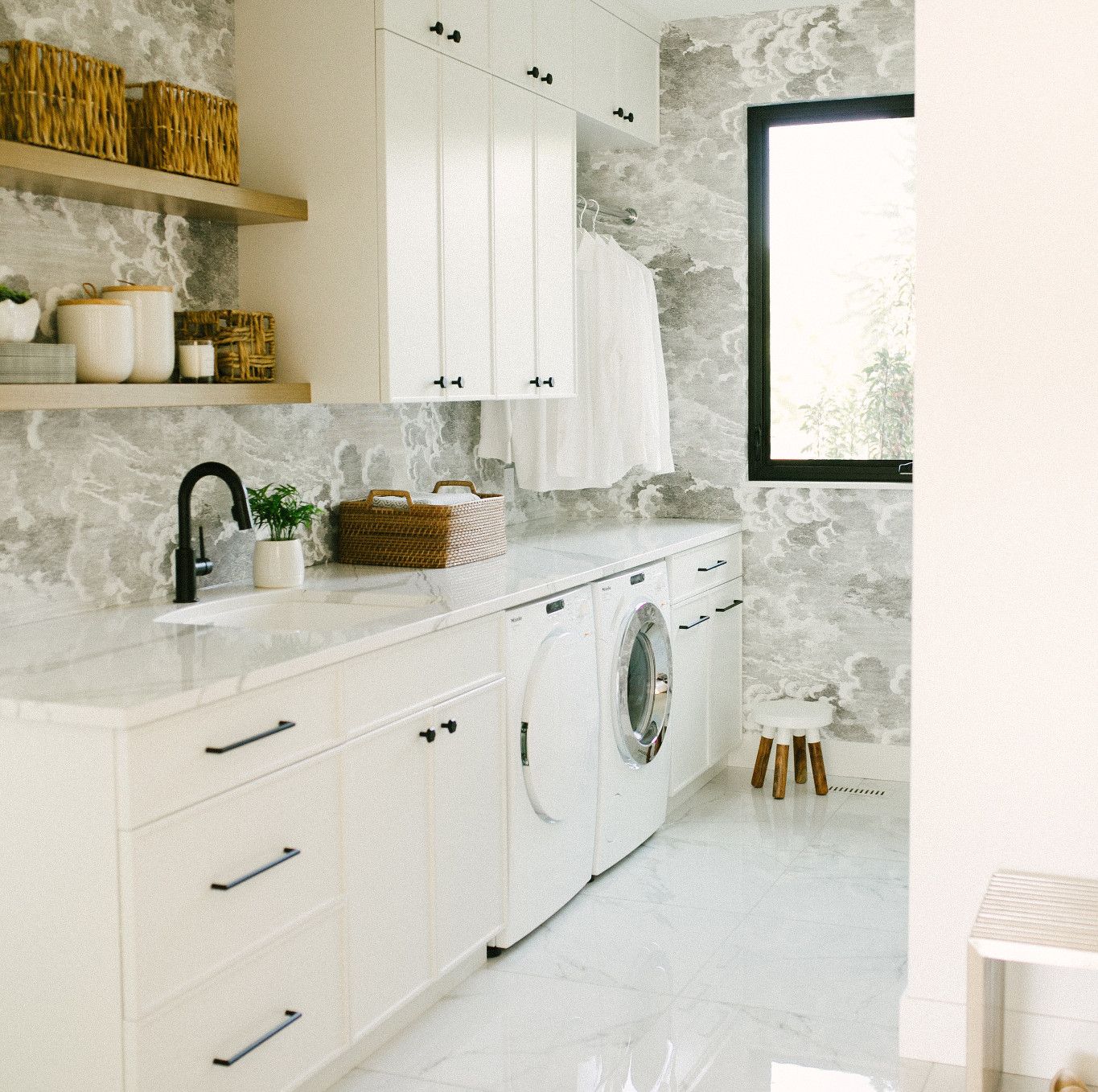 a glistening white laundry room with white countertops, Cambria Brittanicca quartz countertops, open wooden shleving, a sink, and lots of storage space.