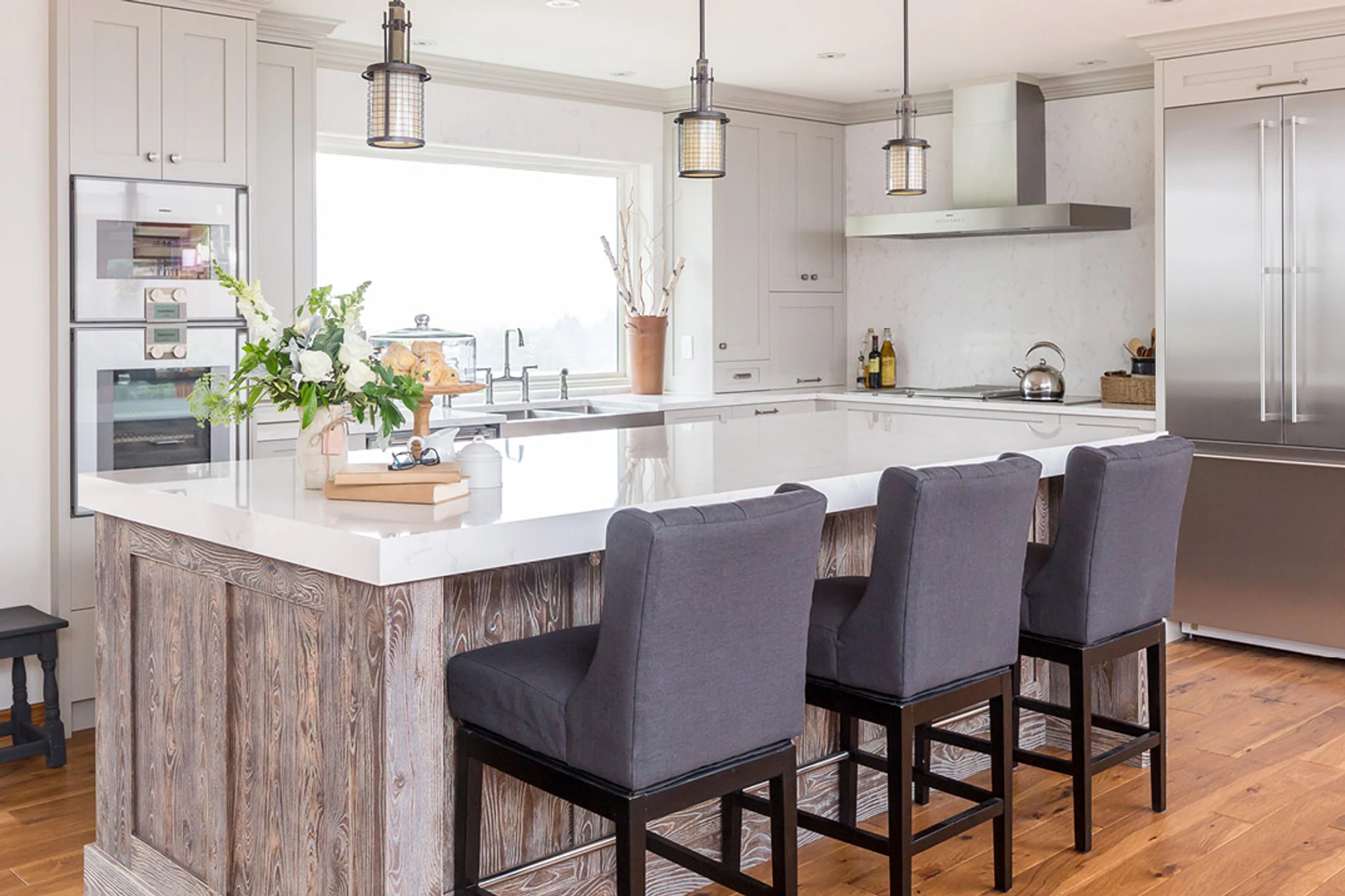 a gorgeous kitchen with a wooden island topped with Cambria Quartz Torquay countertops, three blue barstools, large window over the sink, and modern range.