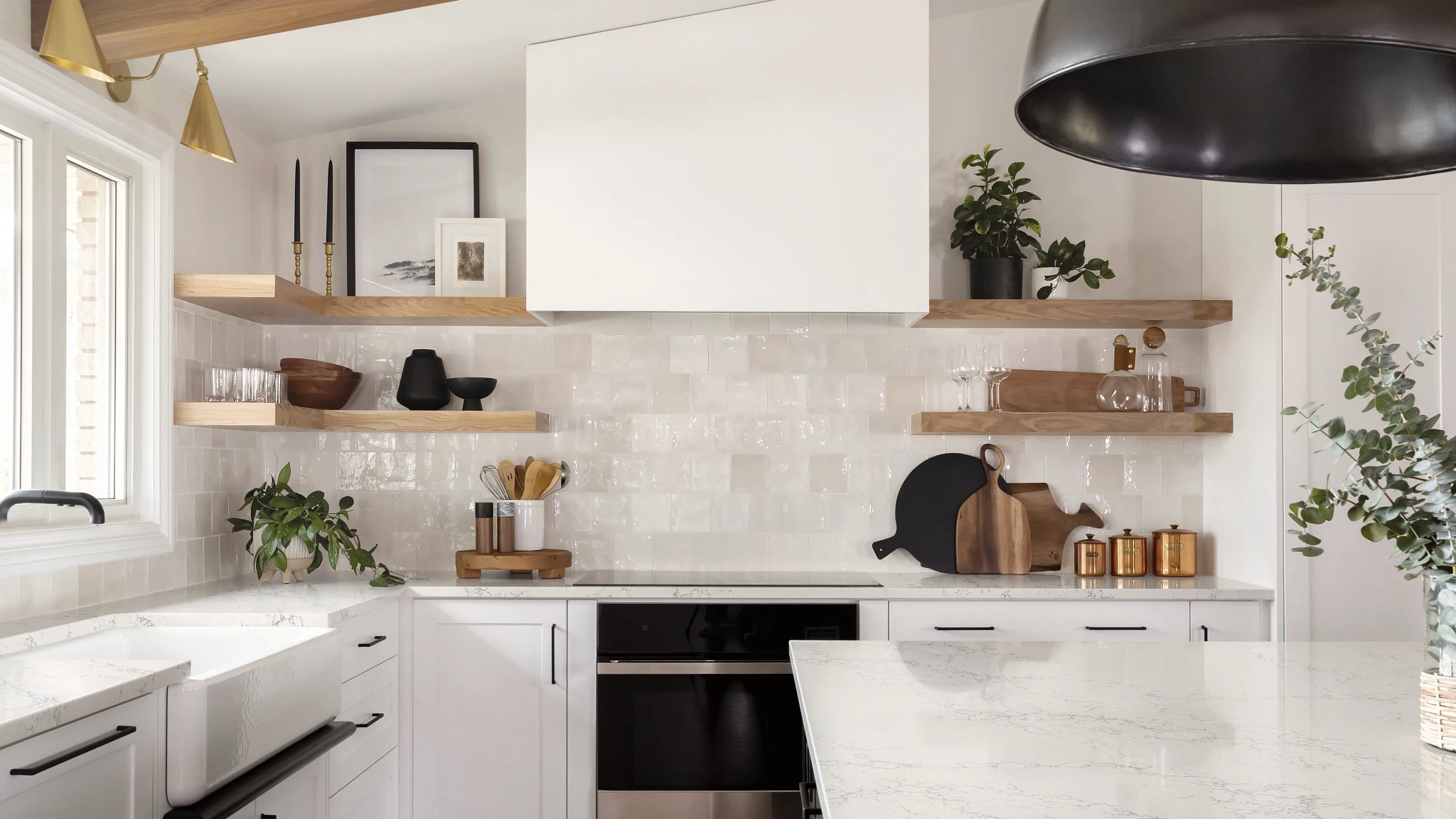 a stunning warm and white kitchen with glossy backsplash tiles, white lower cabinets, with open wooden upper cabinets, a center island, stainless steel appliances, a modern hood over the range, and white quartz countertops. 