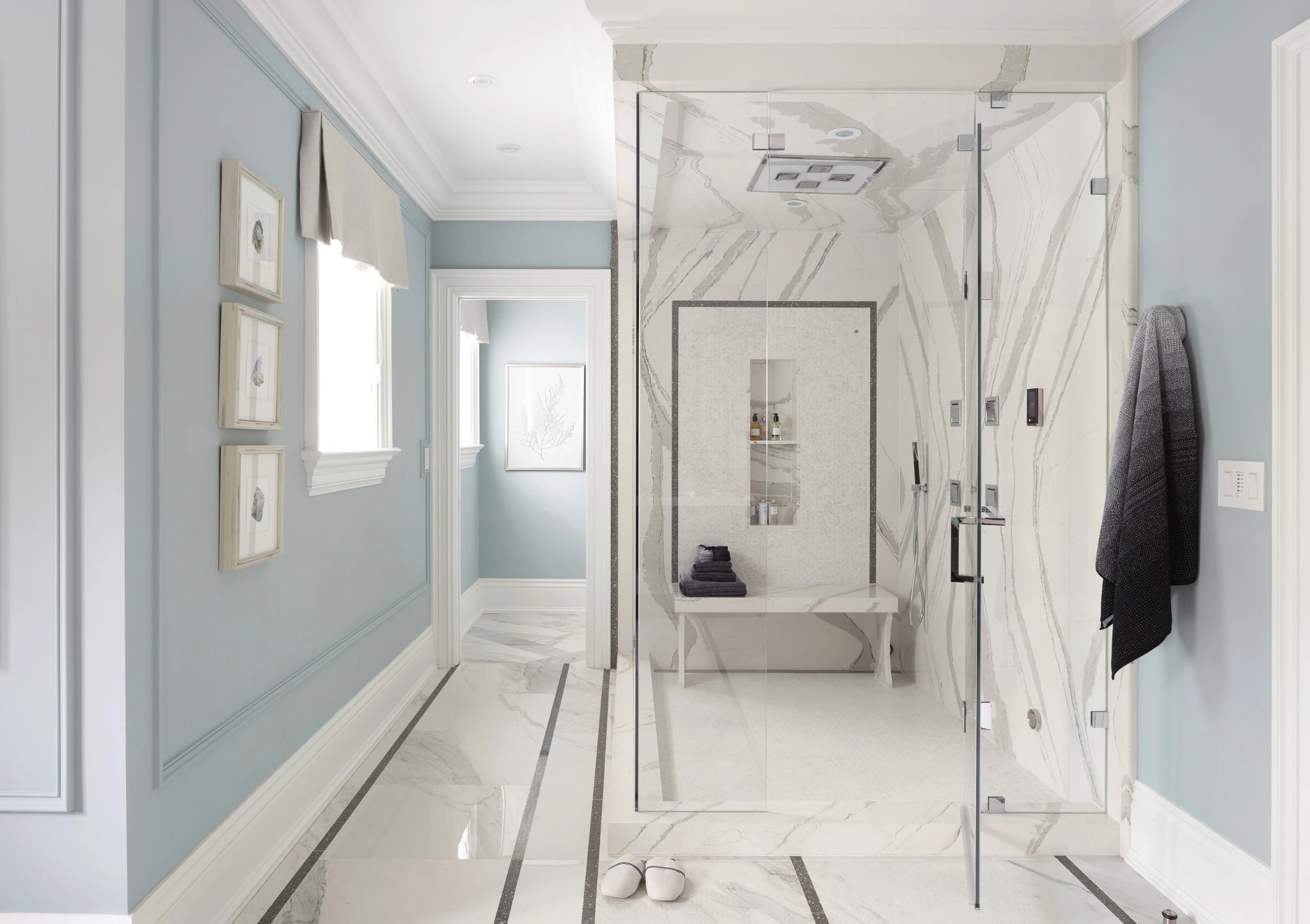 a soothing primary bathroom with Cambria quartz Brittanicca classing on the shower walls, rainfall shower head, and tub deck with baby blue painted walls.