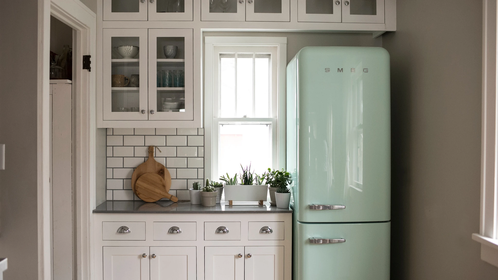 a vintage kitchen with a mint green Smeg fridge, white cabinets, white subway tile, a small window, and Cambria Carrick gray quartz countertops.