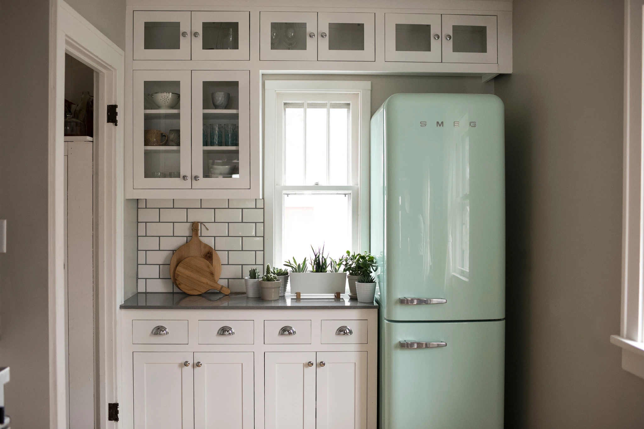 a vintage kitchen with a mint green Smeg fridge, white cabinets, white subway tile, a small window, and Cambria Carrick gray quartz countertops.