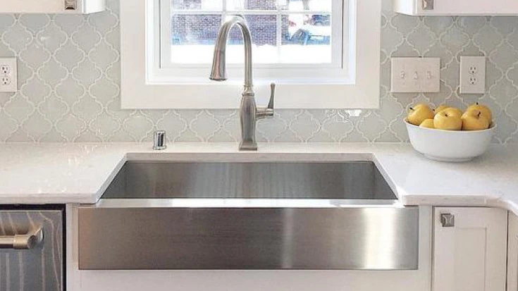 stainless steel farmhouse sink with Swanbridge quartz countertops and a tile backsplash