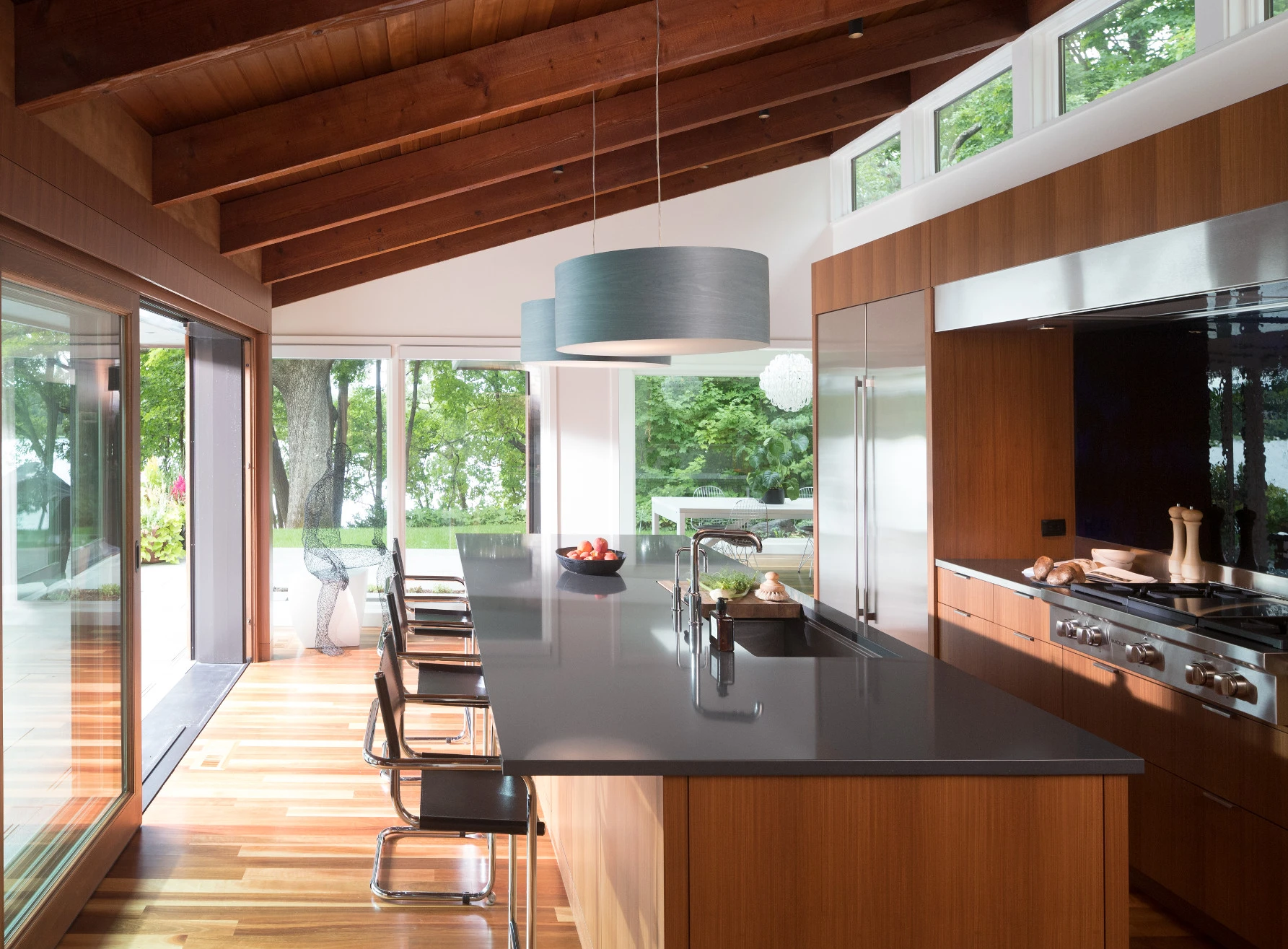 a mid-century modern kitchen by Petersen/Keller Architecture with wooden cabinets, a wooden vaulted ceiling, lots of windows with natural lighting, and a large kitchen island topped with Cambria Fieldstone gray quartz countertops.