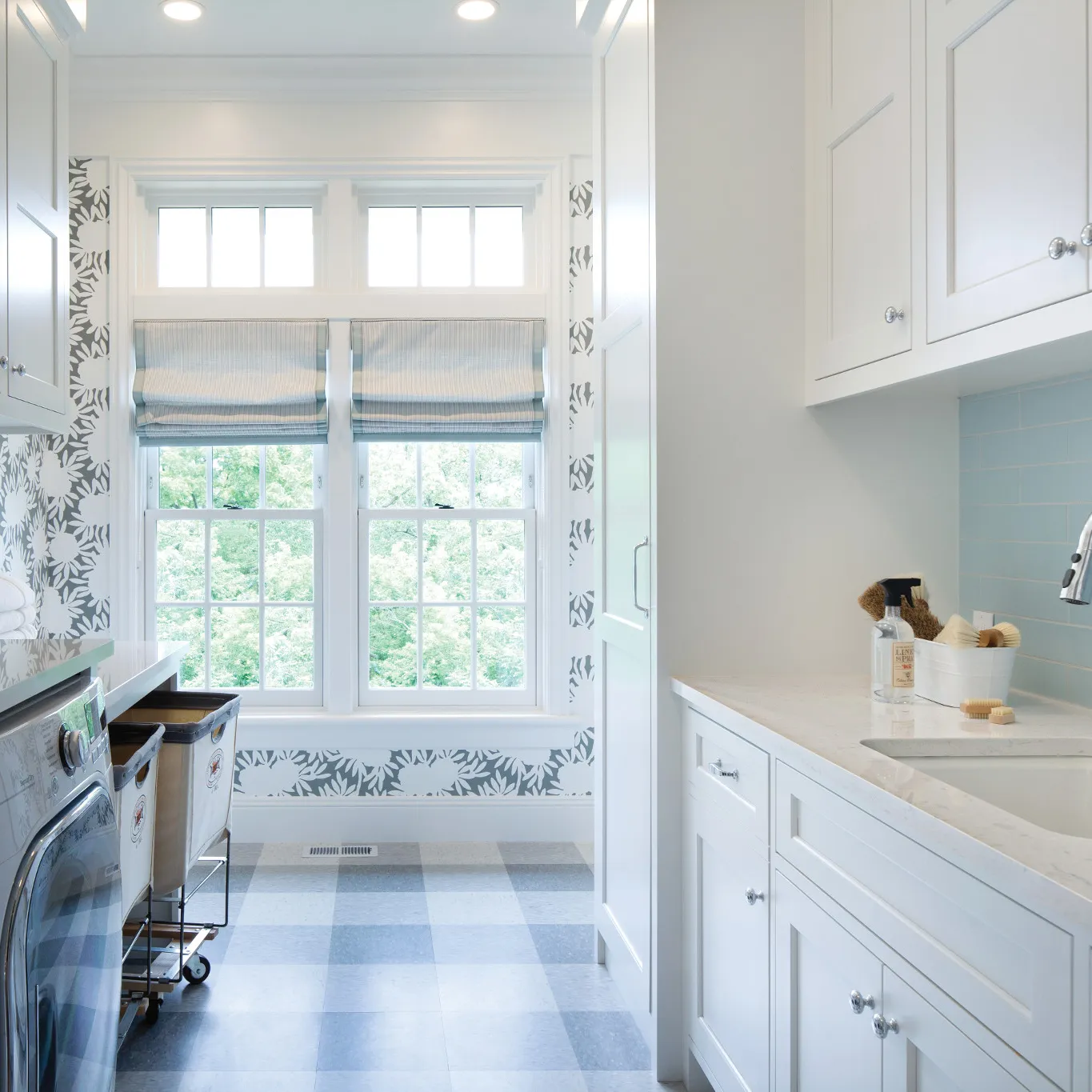 an open and airy laundry room with Cambria Weybourne countertops, blue checkered flooring, playful floral wallpaper, and lots of white cabinetry.